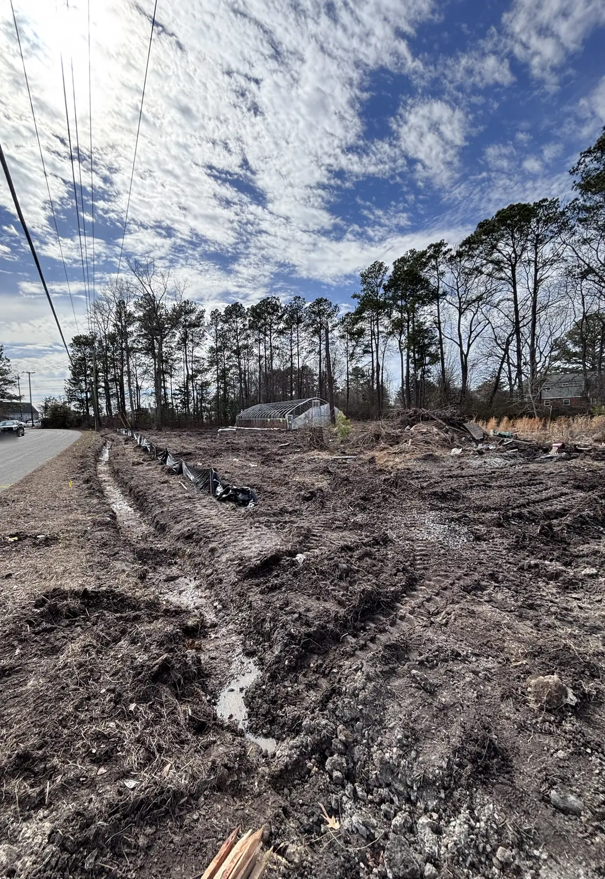 Muddy, rutted cleared ground beside a paved road under power lines